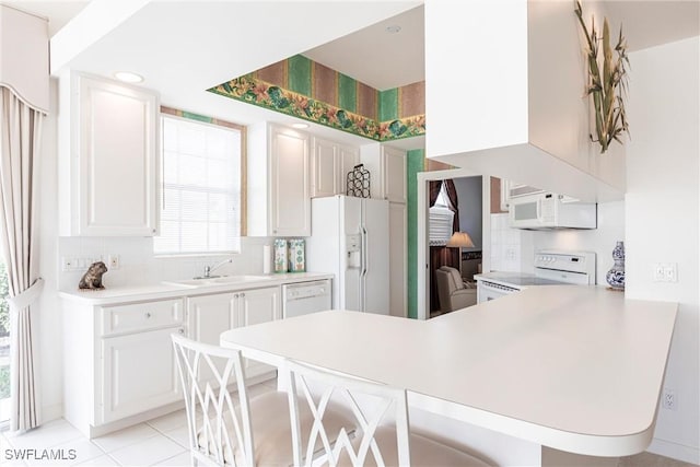 kitchen featuring tasteful backsplash, white appliances, a breakfast bar area, light countertops, and a peninsula
