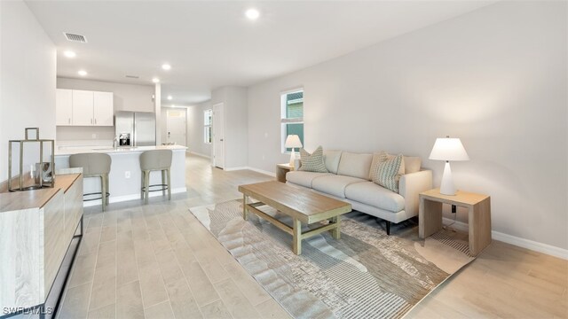 living room featuring light wood finished floors, baseboards, visible vents, and recessed lighting