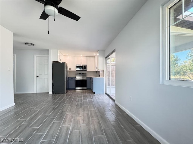 kitchen with baseboards, white cabinets, appliances with stainless steel finishes, wood finish floors, and a sink