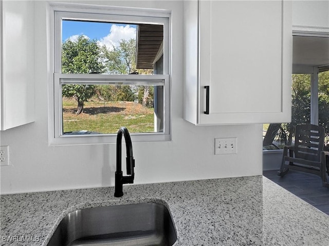 room details with white cabinetry, sink, and light stone counters