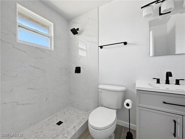 full bathroom featuring baseboards, a tile shower, vanity, and toilet