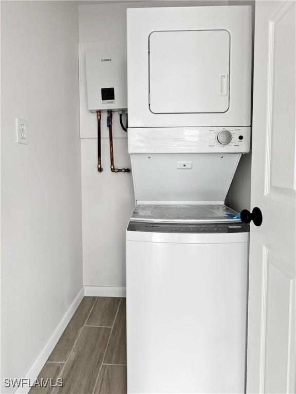 clothes washing area with laundry area, baseboards, water heater, wood tiled floor, and stacked washer and clothes dryer