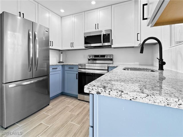 kitchen with stainless steel appliances, a sink, white cabinetry, light stone countertops, and wood tiled floor