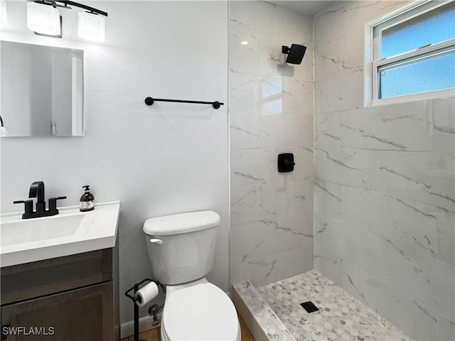 bathroom with toilet, tiled shower, and vanity