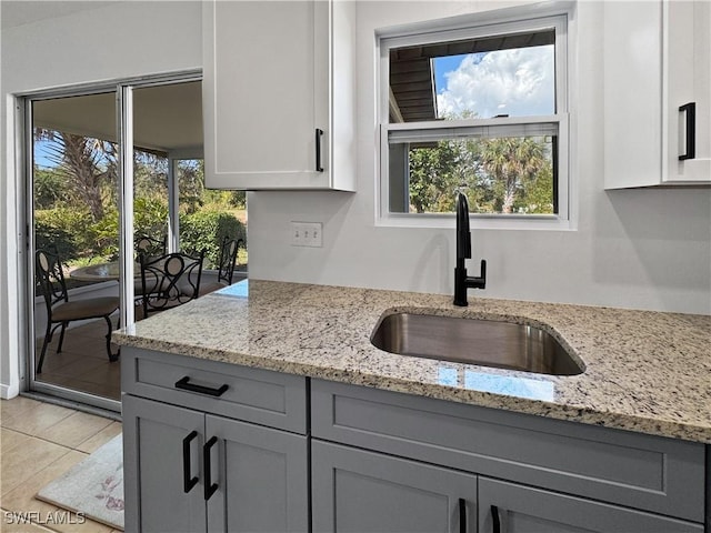 kitchen with plenty of natural light, a sink, light stone countertops, and gray cabinetry