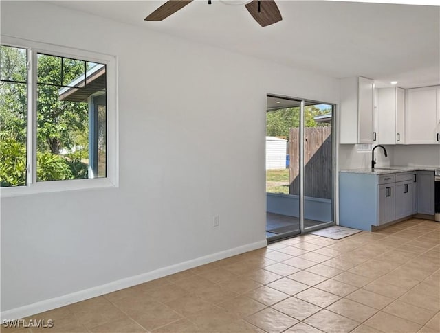 interior space featuring light tile patterned floors, a ceiling fan, baseboards, white cabinets, and light stone countertops