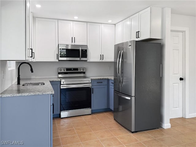 kitchen with white cabinets, appliances with stainless steel finishes, light stone counters, a sink, and light tile patterned flooring