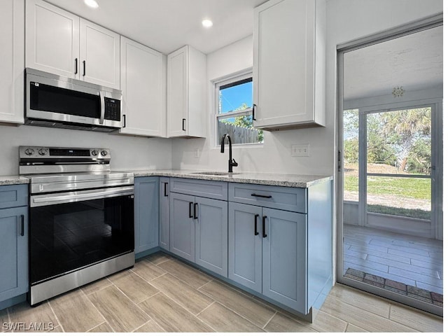 kitchen with recessed lighting, a sink, white cabinets, appliances with stainless steel finishes, and light stone countertops