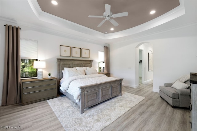 bedroom with crown molding, a tray ceiling, and light wood-type flooring