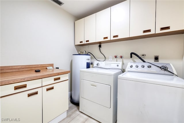 laundry room featuring water heater, washing machine and dryer, light wood-type flooring, and cabinets