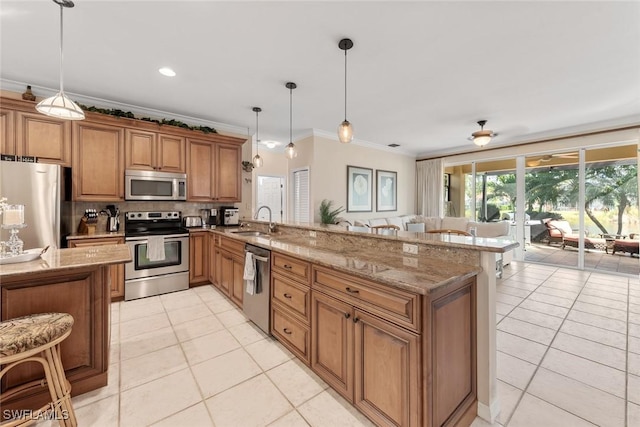 kitchen featuring stainless steel appliances, a peninsula, a sink, brown cabinets, and decorative light fixtures