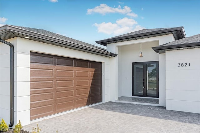 entrance to property featuring a garage, a shingled roof, and stucco siding