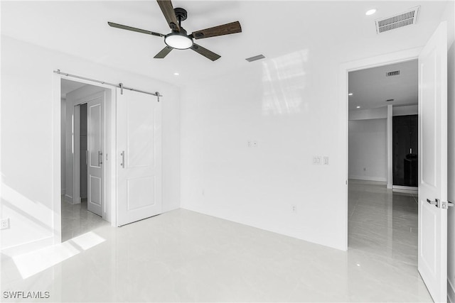 unfurnished room featuring ceiling fan, a barn door, and visible vents