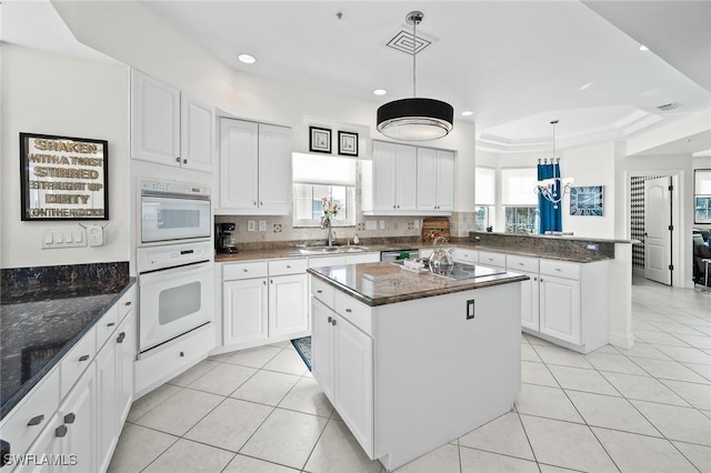 kitchen featuring light tile patterned floors, black electric stovetop, a peninsula, a sink, and a center island