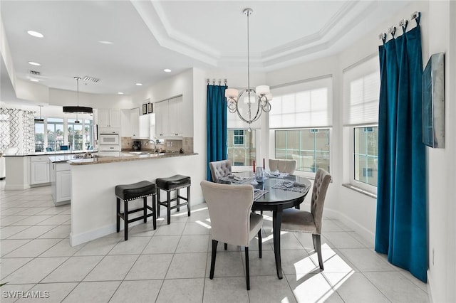 dining area featuring a raised ceiling, a notable chandelier, and light tile patterned floors