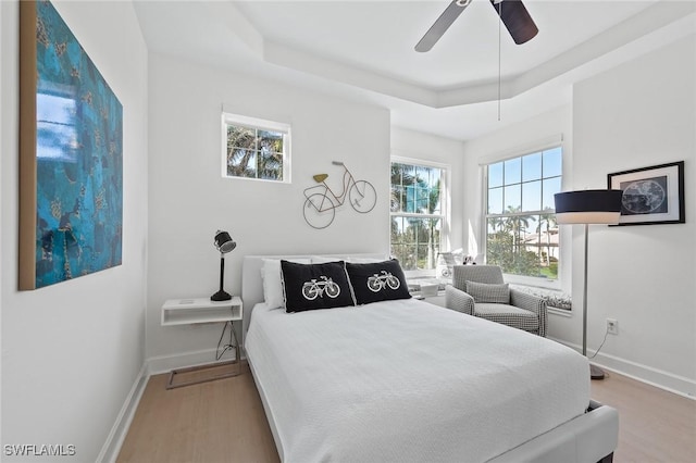 bedroom with ceiling fan, baseboards, a raised ceiling, and wood finished floors