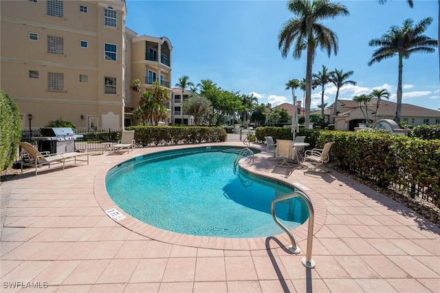 community pool with a patio, grilling area, and fence