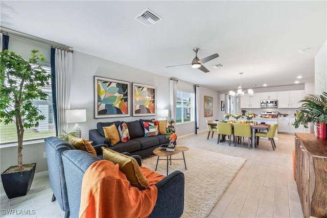 living area featuring light wood-type flooring, baseboards, visible vents, and ceiling fan with notable chandelier