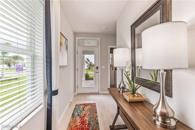 doorway to outside with light wood finished floors, baseboards, and a wealth of natural light