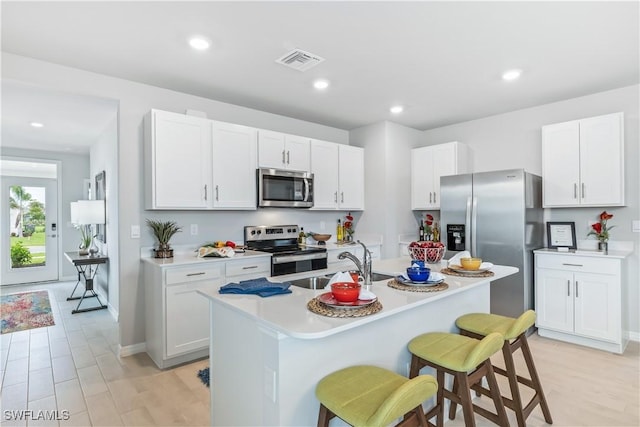 kitchen featuring a center island with sink, visible vents, appliances with stainless steel finishes, a kitchen breakfast bar, and light countertops