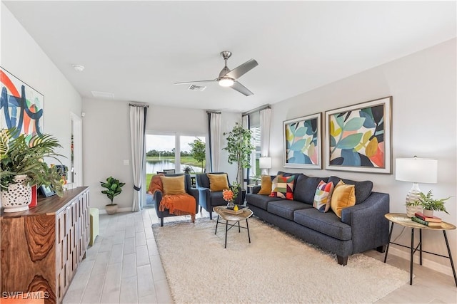 living area with baseboards, visible vents, a ceiling fan, a water view, and light wood-style floors