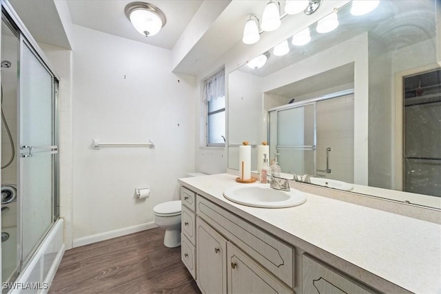 full bathroom with hardwood / wood-style flooring, vanity, combined bath / shower with glass door, and toilet