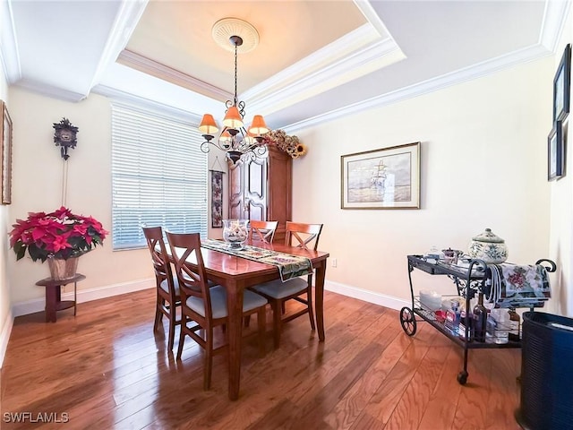 dining space with a raised ceiling, ornamental molding, hardwood / wood-style floors, and an inviting chandelier