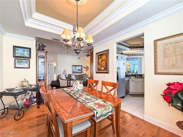 dining area with a raised ceiling, ornamental molding, an inviting chandelier, and light wood-type flooring