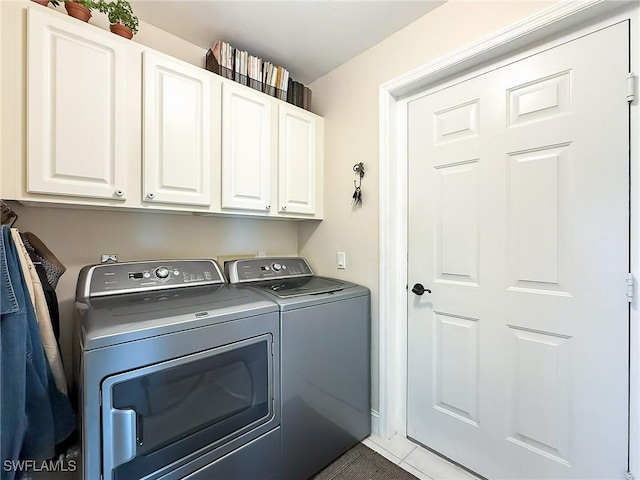 clothes washing area with cabinets, dark tile patterned floors, and washer and clothes dryer