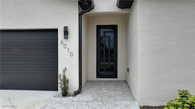 view of exterior entry with stucco siding and a garage