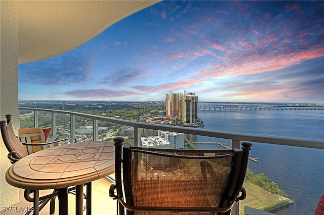 balcony at dusk featuring a water view