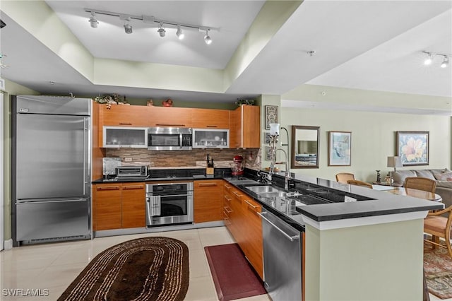 kitchen with decorative backsplash, dark countertops, a peninsula, stainless steel appliances, and a sink