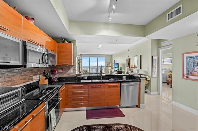 kitchen featuring visible vents, decorative backsplash, appliances with stainless steel finishes, brown cabinetry, and a sink