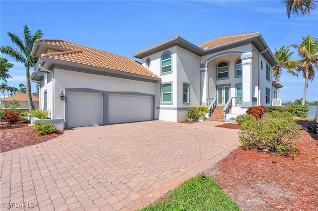 mediterranean / spanish home with a garage, decorative driveway, a tile roof, and stucco siding