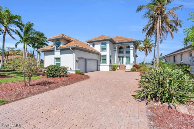 mediterranean / spanish home with a garage, a tiled roof, decorative driveway, and stucco siding