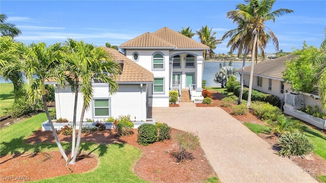 mediterranean / spanish house featuring a tiled roof, decorative driveway, a water view, and stucco siding