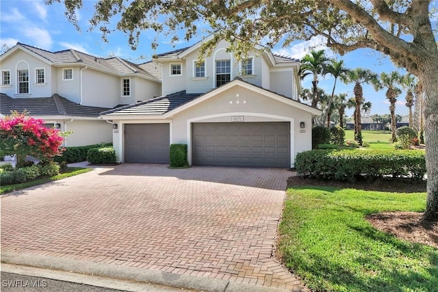 view of front of house with a garage, a tiled roof, decorative driveway, a front yard, and stucco siding