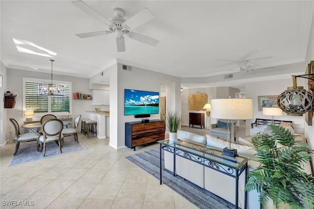 living room featuring light tile patterned floors, baseboards, visible vents, crown molding, and ceiling fan with notable chandelier