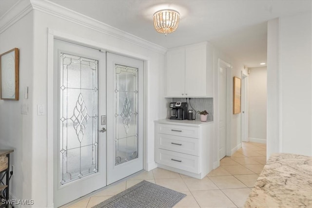 tiled foyer entrance with an inviting chandelier, crown molding, and french doors