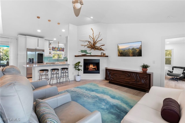 living area with vaulted ceiling, a lit fireplace, light wood-style flooring, and recessed lighting