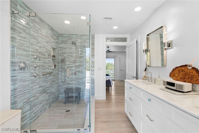 ensuite bathroom with double vanity, a stall shower, visible vents, wood finished floors, and a sink