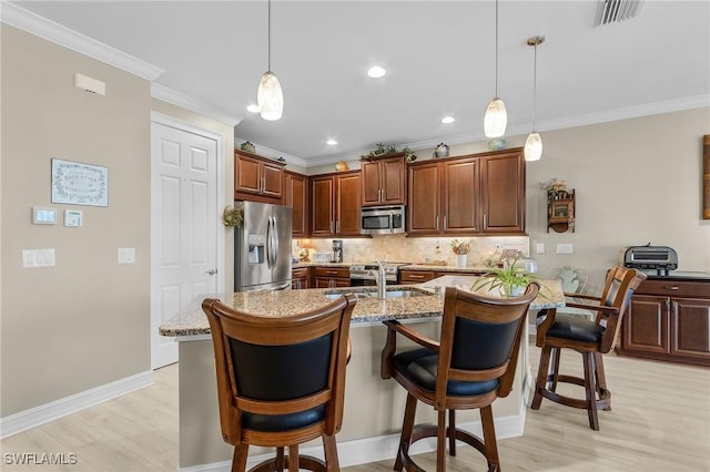 kitchen featuring sink, a breakfast bar area, stainless steel appliances, light stone counters, and decorative light fixtures