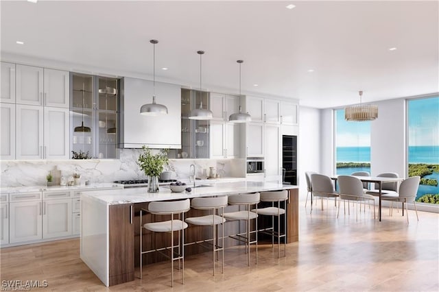 kitchen featuring stainless steel gas cooktop, a large island, light wood-type flooring, backsplash, and glass insert cabinets