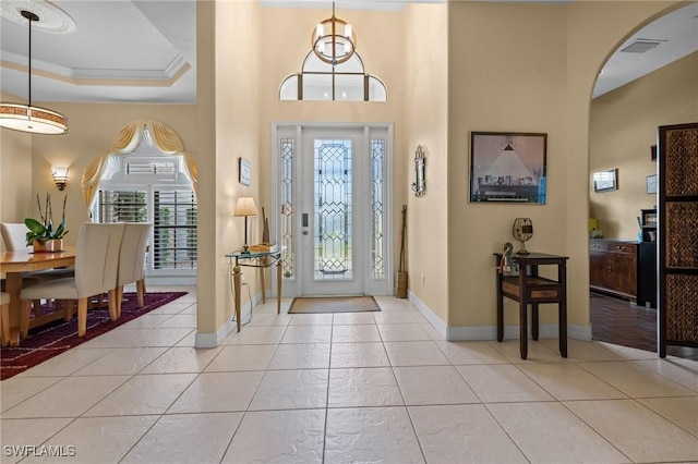 foyer entrance with a raised ceiling, ornamental molding, and light tile patterned floors