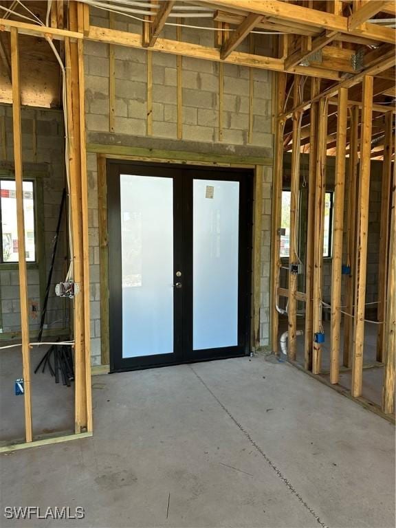 miscellaneous room with concrete block wall, french doors, and unfinished concrete floors