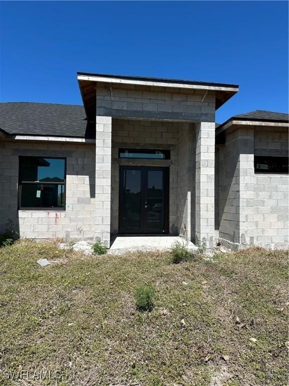 doorway to property featuring a shingled roof, concrete block siding, and french doors