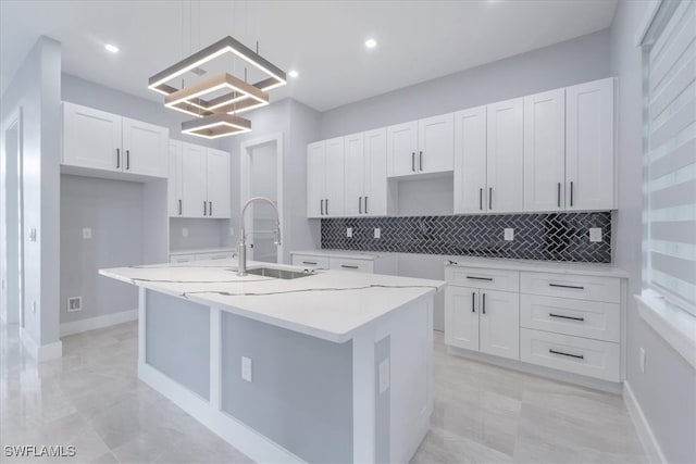 kitchen featuring pendant lighting, sink, white cabinets, and a center island with sink