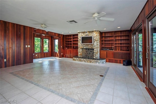 unfurnished living room featuring built in shelves, ceiling fan, wood walls, a fireplace, and light tile patterned floors