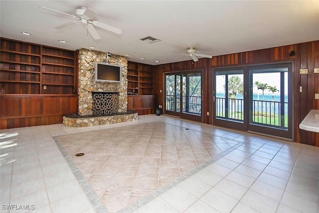 unfurnished living room with light tile patterned flooring, ceiling fan, a fireplace, wooden walls, and built in features