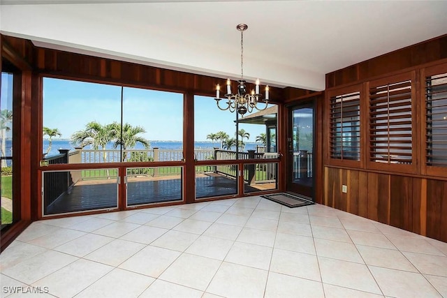 unfurnished dining area with a water view, light tile patterned floors, wood walls, and a notable chandelier